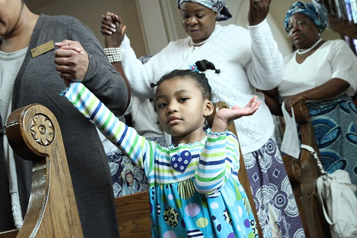 Four-year-old Aren Paige holds her mother’s hand during the praying of the Our Father at the Jan. 14 Martin Luther King Jr. Eucharistic Celebration. It took place at the Shrine of the Immaculate Conception, Atlanta, where she and her mother are members. Photo By Michael Alexander