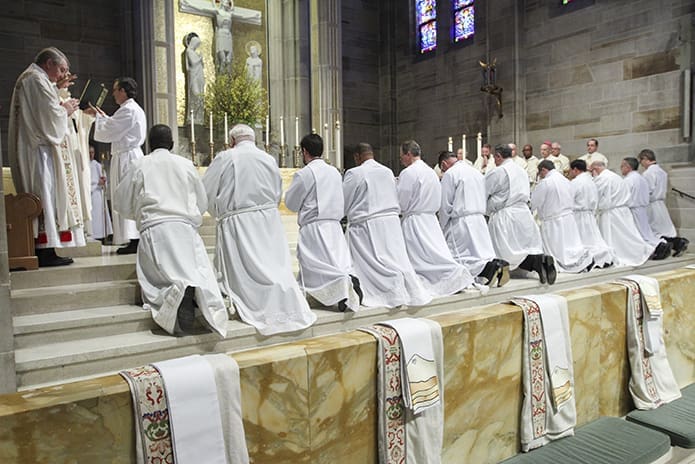 The candidates (l-r) Lennison Alexander, John Halloran, Charles Iner, J. Tony King, Ron Leidenfrost, John Martin, Gregory Orf, Randall Ory, Pablo Perez, Leon Roberts, Erik Wilkinson and Bradford Young kneel on the steps of the altar during the Feb. 4 rite of ordination to the permanent diaconate as Archbishop Gregory conducts the prayer of consecration. Photo By Michael Alexander