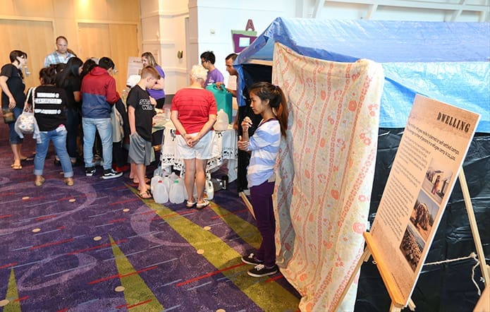 Ti Hniang, foreground, a member of the Catholic Charities Atlanta staff stands by a mock-up of a dwelling as Starve Wars volunteers view the resettlement process for refugees. Hniang, a native of Burma, came to the United States in 2010. Photo By Michael Alexander