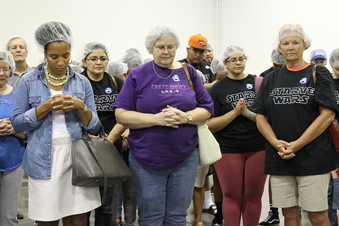 (L-r) Stephanie Williams of the Cathedral of Christ the King, and Nancy Fisher and Cathy Abell of St. George Church, Newnan, pray with other volunteers before they start packing meals. Photo By Michael Alexander