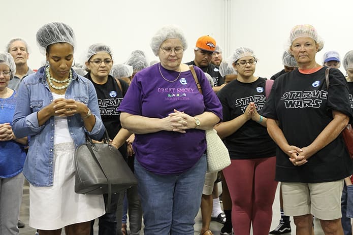(L-r) Stephanie Williams of the Cathedral of Christ the King, and Nancy Fisher and Cathy Abell of St. George Church, Newnan, pray with other volunteers before they start packing meals. Photo By Michael Alexander