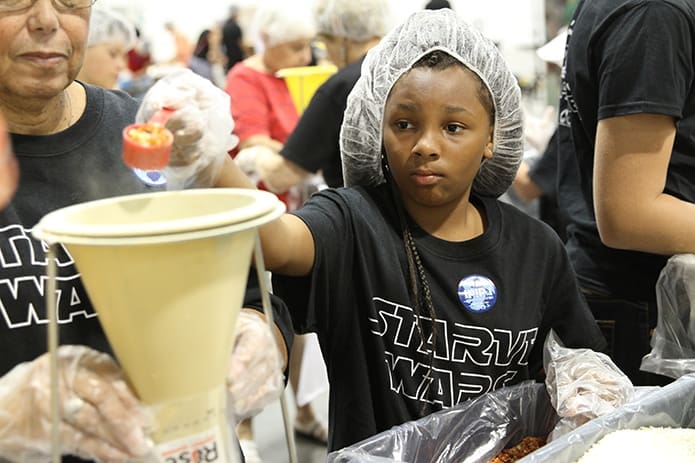 Ten-year-old Quen Daniel helps fill the meal bags as she pours dehydrated vegetables into the funnel. She accompanied her grandmother and older sister to the June 16 service project. Photo By Michael Alexander