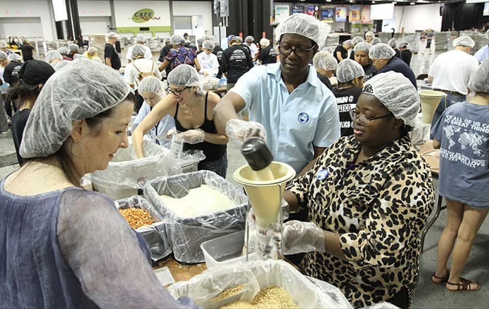 (R-l) Pauline Sawadogo and her husband, Jean, of St. John Neumann Church, Lilburn, work on a team that fills meal bags with soy, rice, dehydrated vegetables and a vitamin pack. The couple originally hails from Burkina Faso. In the background on the same side of the table, Natalie Lewis of Holy Spirit Church, Atlanta, and her daughter Dominique, 10, work with another team. Lewis was also accompanied by her sons, eight-month-old Sebastian and eight-year-old Alexander. Photo By Michael Alexander