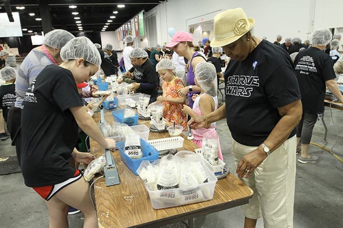 Jamie Martin, left, a rising sophomore at St. Pius X High School, Atlanta, seals the meal bags as Jeanne Mosley of Most Blessed Sacrament Church, Atlanta, works at the scale, making sure the meal bags weigh between 389 and 394 grams. Photo By Michael Alexander