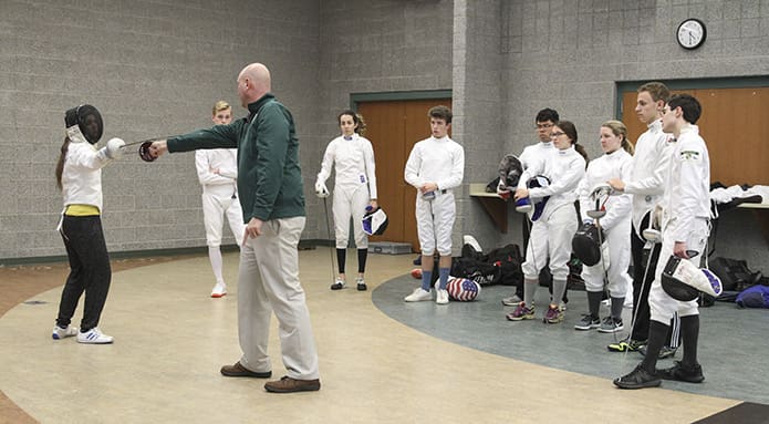 As members of the team look on, Pinecrest Academy head fencing coach Chad Morris, foreground in green jacket, demonstrates why distance matters during fencing with senior fencer Claire Rivard. Practice is held at the Old Atlanta Recreation Center in Suwanee. Photo By Michael Alexander