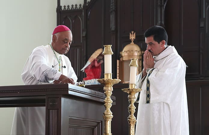 Archbishop Wilton D. Gregory, left, pours sacred oil on the altar as he prepares to anoint it. Looking on from the right is Deacon Jose Pineda. Photo By Michael Alexander
