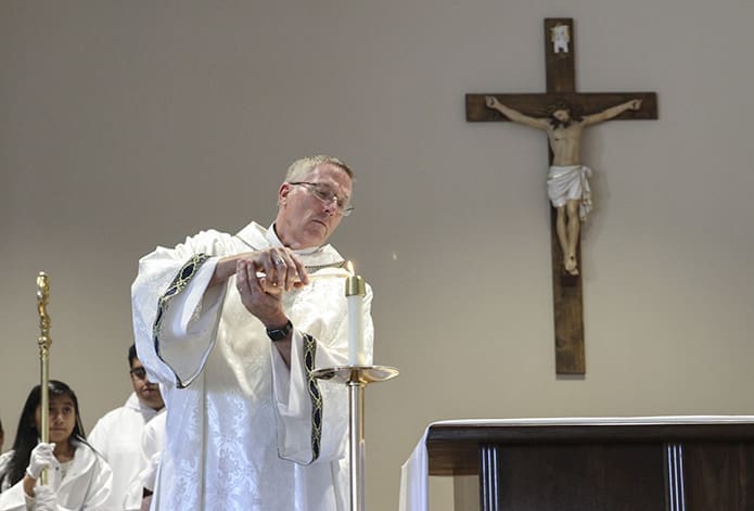 Deacon Tom Ryan lights the candles on the altar before the Liturgy of the Eucharist. Photo By Michael Alexander