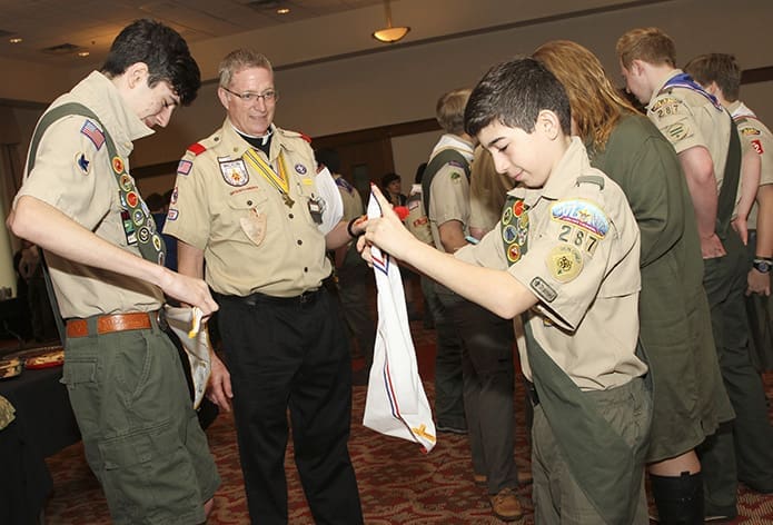 Deacon Tom Ryan, second from left, the chaplain for St. Catherine of Siena Church’s Troop 422, watches as Thomas Kent, left, and his younger brother, Matthew, of St. Joseph Church’s Troop 287, Marietta, prepare their neckerchiefs before the March 24 Atlanta Archdiocesan Scout Mass. Photo By Michael Alexander