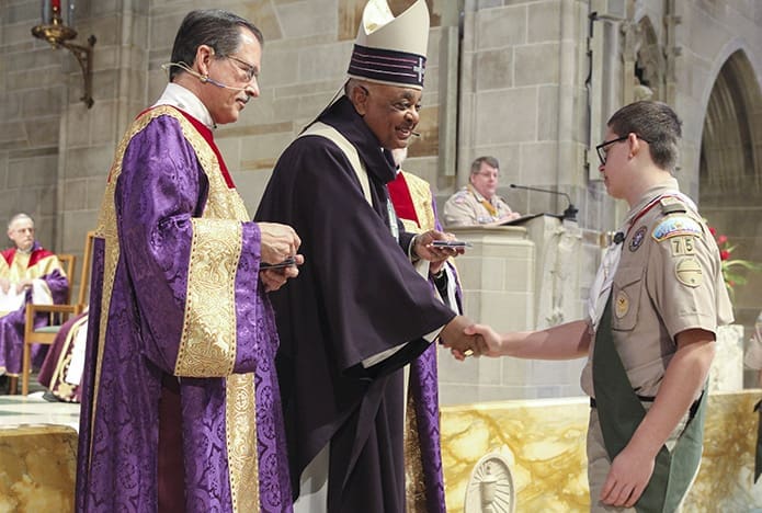 Archbishop Wilton D. Gregory shakes the hand of DJ Peyroux from Transfiguration Church’s Troop 75, just before presenting the Ad Altare Dei emblem to him. The Ad Altare Dei program is designed to help the scout grow in knowledge and appreciation of the sacraments. Forty-seven scouts received the emblem this year and eight were from Troop 75. Photo By Michael Alexander