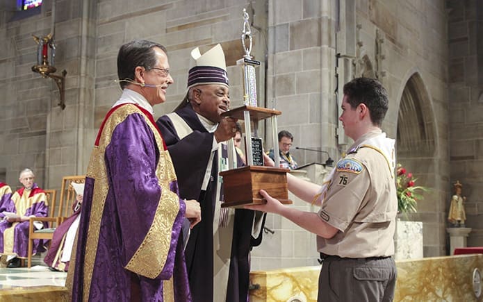 Archbishop Wilton D. Gregory presents the Bishop’s Trophy to Nick McFadden from Transfiguration Church’s Troop 75. Looking on is Deacon Tom Gotschall, left, chaplain for the Archdiocesan Catholic Committee on Scouting. Photo By Michael Alexander