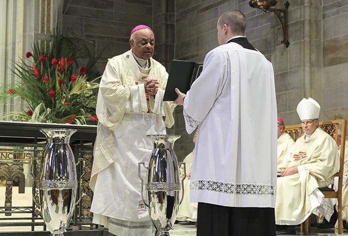 Standing on the altar of the Cathedral of Christ the King, Atlanta, Archbishop Wilton D. Gregory, left, leads a prayer for the blessing of the oil of the sick during the March 27 Chrism Mass, as seminarian Robbie Cotta holds the Roman Pontifical. Photo By Michael Alexander
