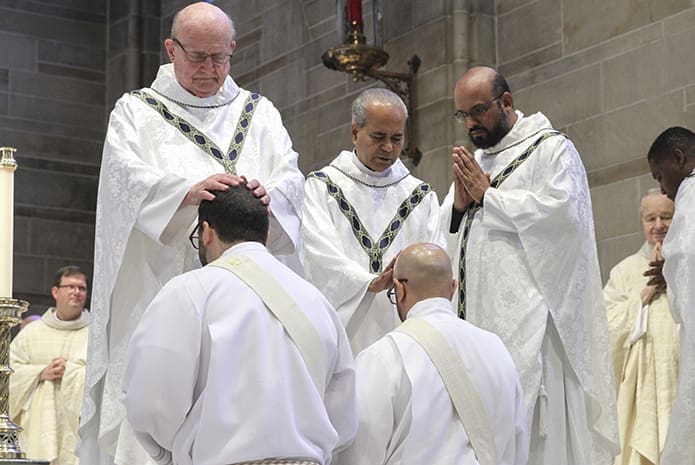 Senior priest Father Anthony Curran, top left, and Missionaries of St. Francis de Sales Father Joseph Mullakkara, top center, parochial vicar at St. Benedict Church, Johns Creek, lay hands upon ordination candidates Jack Knight and Carlos Ortega, respectively. Waiting his turn is Father Gaurav Shroff, top right, parochial vicar at St. Andrew Church, Roswell. Photo By Michael Alexander