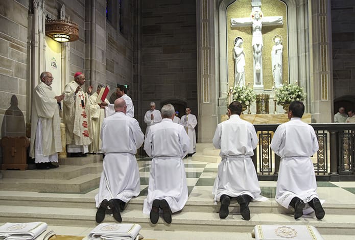 Four of the eight ordination candidates, (foreground, l-r) Timothy Dimond, Stephen Gross, Thomas Nemchik and Guillermo Hedy Sevilla, can be seen kneeling before the altar as Archbishop Wilton D. Gregory conducts the prayer of consecration. Photo By Michael Alexander