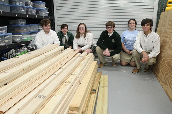 (L-r) Senior Dylan Uhrik, sophomores Robert Della Bernarda, Kat Montgomery and Aidan Vick, senior Rosie Nemec and sophomore Eli Gearheard squat down by some of the donated lumber for the tiny home build project stored in the school's STEAM (Science, Technology, Engineering, Art and Mathematics) lab. Photo By Michael Alexander