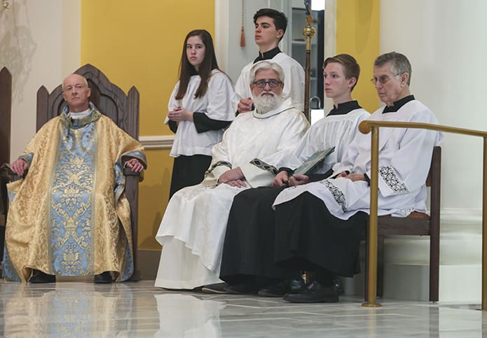 (Seated, l-r) Father Darragh Griffith, the current pastor of Mary Our Queen Church, Peachtree Corners, Deacon Robb Ciezki of the Diocese of Buffalo, altar server Ethan Brown and Ric Liegerot, assistant master of ceremonies, wait on the altar and look out over the congregation during the incensation of the church. Photo By Michael Alexander