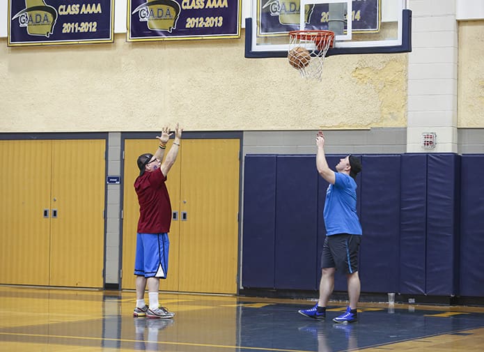 Core member Terry Hochschild, left, hits two of his 112 points during L’Arche Madness at Marist School’s Centennial Center. L’Arche Atlanta executive director Tim Moore, right, helps Hochschild retrieve the basketballs. Photo By Michael Alexander