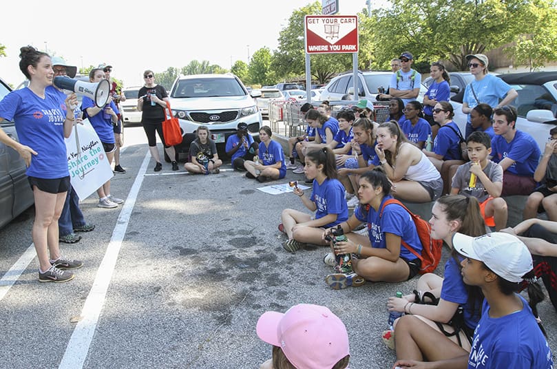 Marist School Share the Journey moderator and campus minister Bernadette Naro, holding the megaphone, gives some final instructions before the group prepares to leave the Dekalb Farmers Market parking lot and resume the next leg of their five-mile walk. Photo By Michael Alexander