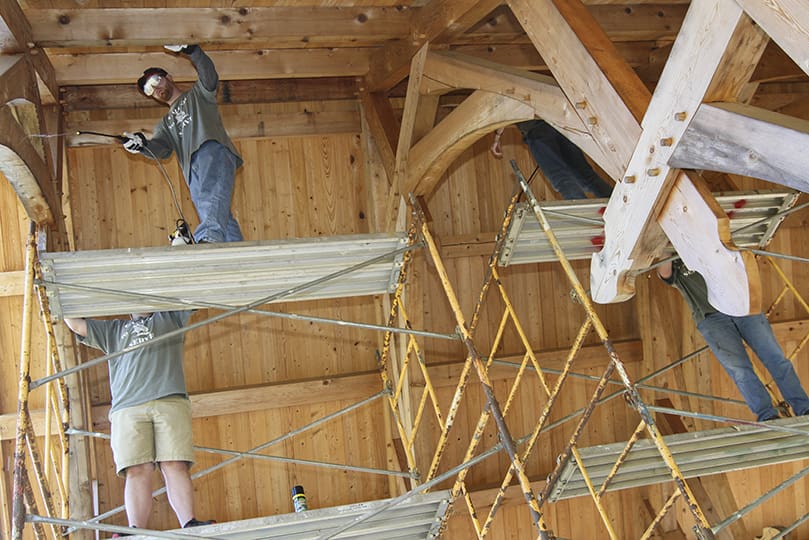 Standing on the scaffold, Deacon Paul Porter, top left, sprays sealant on the wood beams and ceiling before they follow that up with a coat of stain. It was one of the tasks undertaken during a May 16 seminarian workday on the natural burial grounds of Honey Creek Woodlands, Conyers. Photo By Michael Alexander