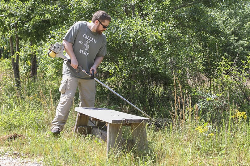Seminarian Ben Thomsen uses the gas trimmer to clear unwanted brush and weeds around the burial plots. Thomsen was one of nearly 20 seminarians participating in a workday at the natural burial grounds of the Monastery of the Holy Spirit’s Honey Creek Woodlands, Conyers. Photo By Michael Alexander