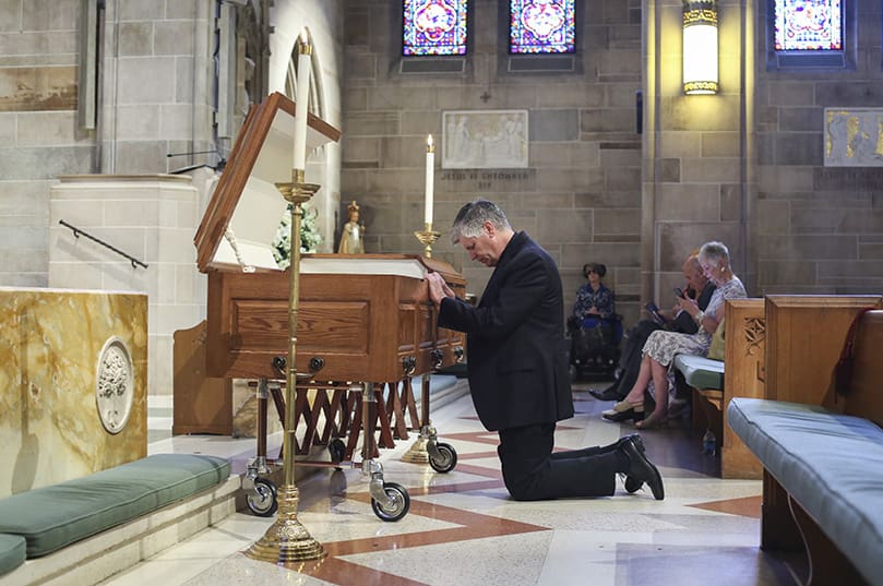 In the center aisle at the Cathedral of Christ the King, Atlanta, some 30 minutes before the June 25 funeral Mass, Bishop Bernard E. Shlesinger III kneels down to say a prayer before the open casket of Father Richard Morrow. Photo By Michael Alexander