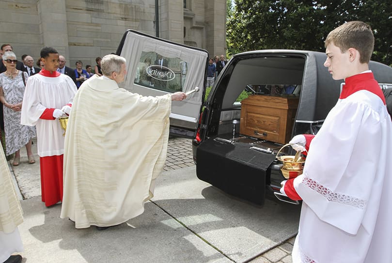 Before the funeral hearse heads off to Arlington Memorial Park in Sandy Springs for the burial, senior priest Msgr. Patrick Bishop, one of the six pall bearers, sprinkles Father Richard Morrow’s casket with holy water like the numerous priests who went before him. Photo By Michael Alexander
