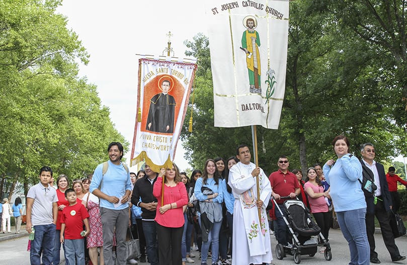 Joined by members of St. Joseph Church, Dalton, Father Duvan Gonzalez, parochial vicar, carries the banner for the parish, which came about 100 miles to attend the 24th annual Eucharistic Congress at the Georgia International Convention Center. Photo By Michael Alexander