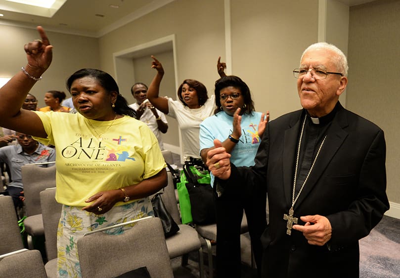 Bishop Guy A. Sansaricq, retired auxiliary bishop for the Diocese of Brooklyn, joins Francophone participants during a moment of praise and worship. Bishop Sansaricq, 84, was the featured speaker during the June 21 Francophone track at the Marriott Gateway Hotel. He is a native of Jeremie, Haiti. Photo By Johnny Crawford