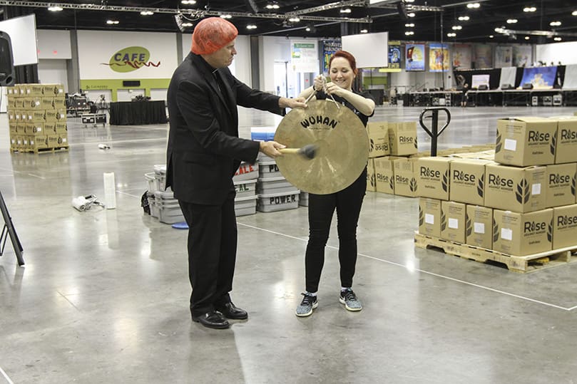 Jayna Hoffacker, right, program assistant for the Justice & Peace Ministries office, holds the Wuhan wind gong as Bishop Bernard E. Shlesinger III sounds it with the mallet to mark the 10 millionth meal packaged through Catholic Relief Services’ Helping Hands program for the country of Burkina Faso in Africa. Photo By Michael Alexander