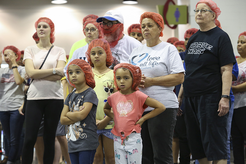 (Counter-clockwise, from top, center-right) Marlene Arce, her husband Pedro, and their granddaughters, nine-year-old Hailey and six-year-olds Katherine and Taylor, listen to instructions for meal packing during the second session of Starve Wars. Photo By Michael Alexander