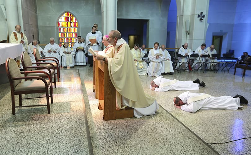 (Center, foreground to background) Abbot Augustine Myslinski, OCSO, and Bishop Joel M. Konzen, SM, kneel in prayer as the ordination candidates to the priesthood, (foreground to background) Brother Peter Damian, OCSO, and Brother Cassian Russell, OCSO, prostrate themselves before the altar during the Litany of Saints. The two monks were ordained at the Monastery of the Holy Spirit, Conyers, June 28. Photo By Michael Alexander