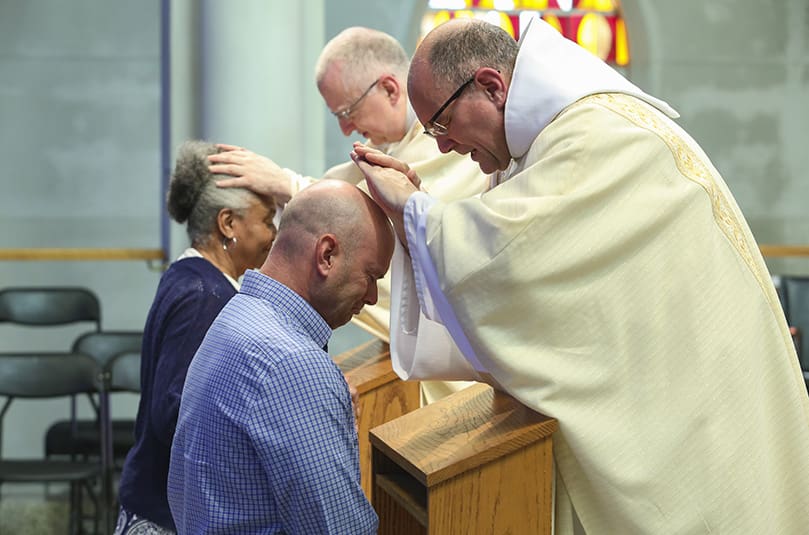 Both are overcome with emotion as the newly ordained Father Peter Damian, OCSO, extends a blessing to his brother, Dave, a resident of Charlotte, North Carolina. In the background, the other recently ordained priest, Father Cassian Russell, OCSO, offers a blessing to a woman. Photo By Michael Alexander