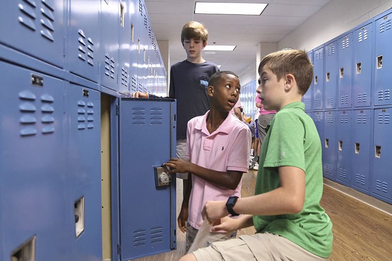 After receiving some tutelage from returning students, Daniel Barber, right, and Alec Devlin, standing, Joseph Contreras, center, a new student at Holy Redeemer School, looks back toward his parents upon successfully opening his school locker. Photo By Michael Alexander