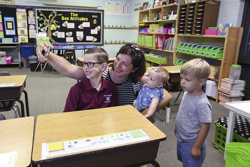 Smartphones and selfies go hand in hand on the first day of school. Andrea Schmidt takes one with her son Owen, a first-grader in Olga Hicksâ class at St. John Neumann Regional School, Lilburn. Looking on and standing by are younger siblings Ellie, seven-months-old, and two-year-old Jake. Owen also has an older brother in the schoolâs fourth grade. Photo By Michael Alexander