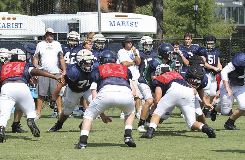 The Marist School football team practices on campus just days before its Aug. 16 preseason scrimmage against McDonough’s Eagles Landing Christian Academy. Observing in the background, wearing white T-shirts, are Paul Etheridge, left, offensive coordinator, and Jim Showfety, center, the running backs coach. Photo By Michael Alexander