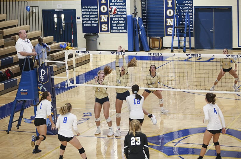 L-r, far side of net) After St. Pius' Lura Underwood (#2) and Annemarie Rakoski (#18) block a shot, Ava Pitchford (#16) waits to hit the volleyball on the rebound. Photo By Michael Alexander