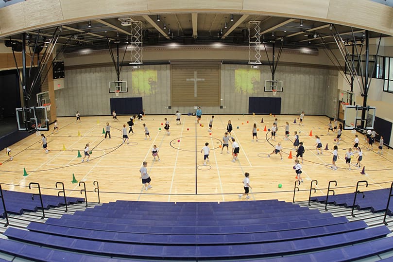Students make use of the gymnasium inside the Cathedral of Christ the King's new Hyland Center during a physical education class. The wood surrounding the cross below is from the bleachers in the original Hyland Center. Photo By Michael Alexander