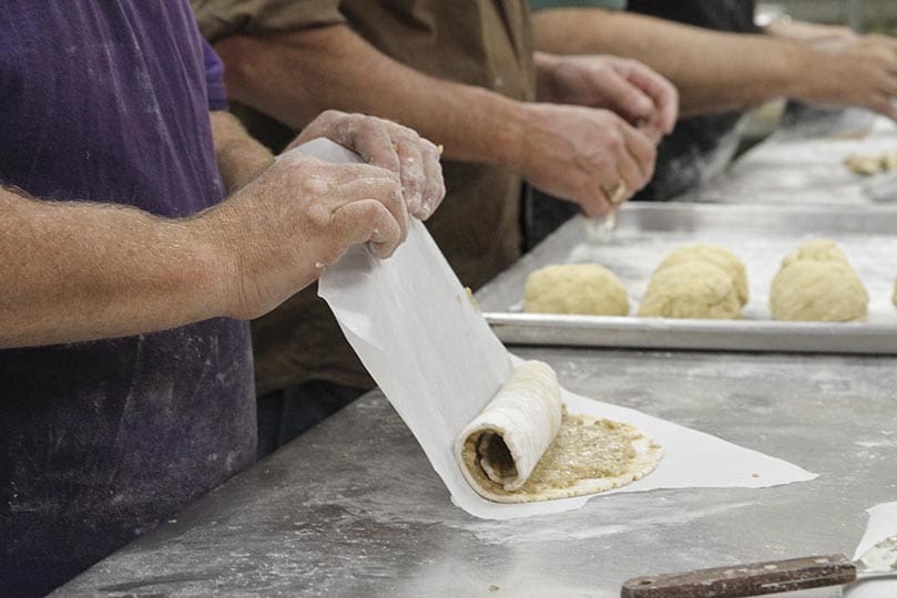 After walnut filling is spread over the dough, Louis Thibodeaux rolls up the dough. Thibodeaux and his neighbor kneading the dough, Joe Cofelice, were first-time participants in the Polish nut rolls project. Photo By Michael Alexander