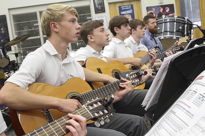 Brion Kennedy, far end, sits with some students in the beginning classical guitar class as they play The Eagles song, 