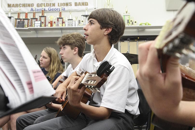 (Foreground to background) Freshmen Andrew Mattei and Paul Van Rooijen and senior Paulina Rey look up at the video screen as they work on barre chords in the beginning classical guitar class. Photo By Michael Alexander