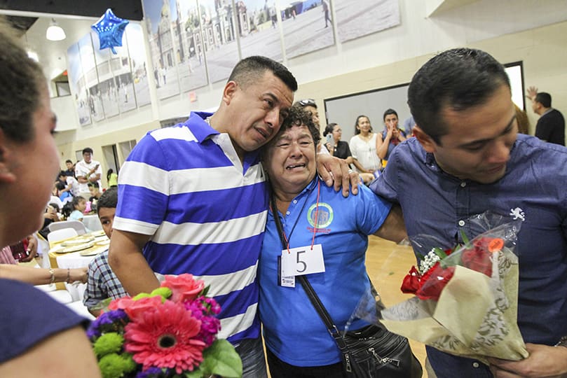 Alejandro Cruz Pena, left center, hugged his mother, Francisca Pena, during a tearful reunion last August at Our Lady of the Americas Mission, Lilburn. On the other side of Alejandro’s mother, holding a bouquet of flowers for her, is his younger brother Raul. Nearly two decades had passed since they last saw their mother. She was one of 44 parents granted temporary visas, so they could spend 20 days with their children and their families. Photo By Michael Alexander
