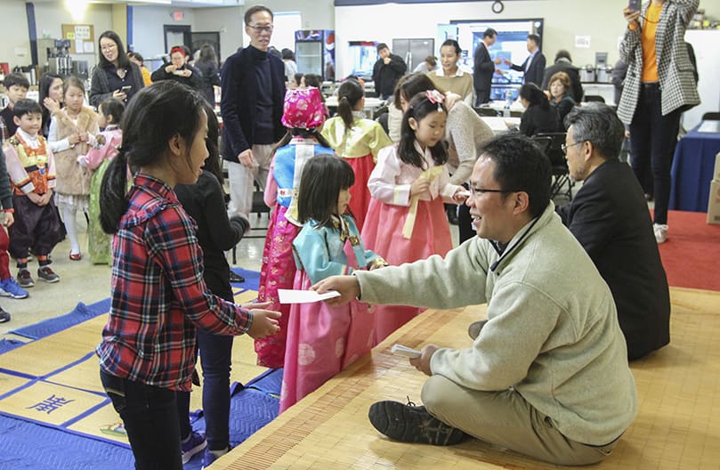 (Sitting on the stage, foreground to background) St. Andrew Kim Church parochial vicar Father Juchan Kim and pastor Father Kolbe Man Young Chung distribute envelopes, enclosed with a two-dollar bill, to the children for good luck in the New Year. Photo By Michael Alexander
