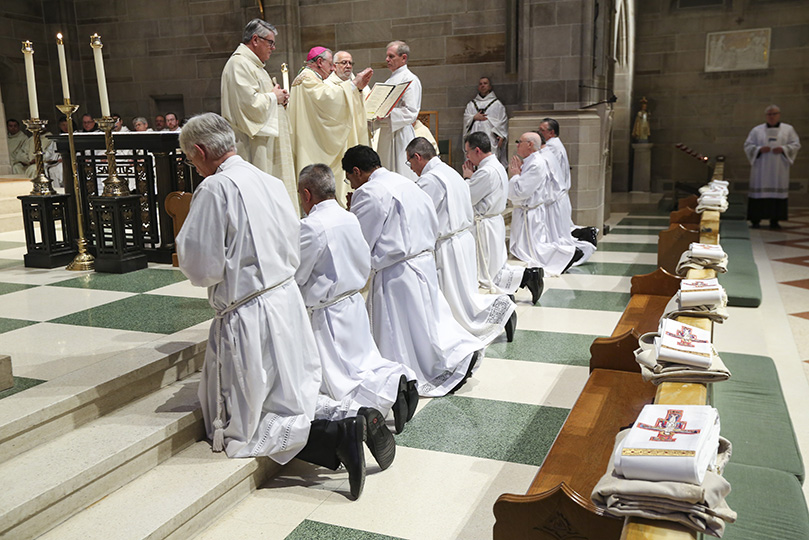 The eight permanent diaconate ordination candidates, (foreground, l-r) Bruce Goodwin, David Hernández, Dev Lobo, Igor Ponce, James Windon, Joseph Odom Jr., William Kester and James Grebe, kneel before the altar as Bishop Joel M. Konzen, SM, the diocesan administrator, conducts the prayer of consecration. At the prayerâs conclusion, the men officially become permanent deacons. Photo By Michael Alexander
