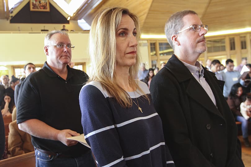 During the presentation of candidates for the Rite of Election and the Call to Continuing Conversion at St. Catherine of Siena Church, Kennesaw, sponsor Cassy Dellinger, center, stands with her husband Jay, right. The Dellingers and the sponsor standing behind them, Michael Smith, belong to Saint Clare of Assisi Church, Acworth, which has 14 candidates and four catechumens this year. Photo By Michael Alexander