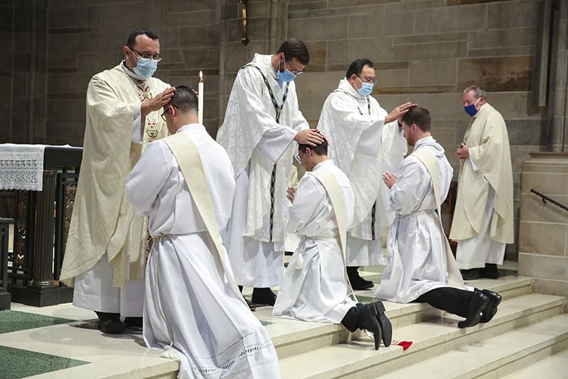 After the archbishop laid hands on each of the three ordination candidates, the priests in the congregation came up to lay hands on the young men. The action signifies conferral of God’s Holy Spirit. Photo By Michael Alexander