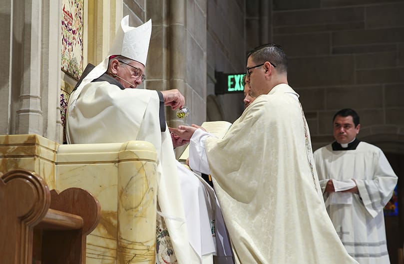 As a sign of the new priest’s ministry to heal, sanctify and offer prayer for God’s people, Archbishop Gregory J. Hartmayer, OFM Conv., left, anoints the hands of Father Cristian Cossio with chrism. Photo By Michael Alexander