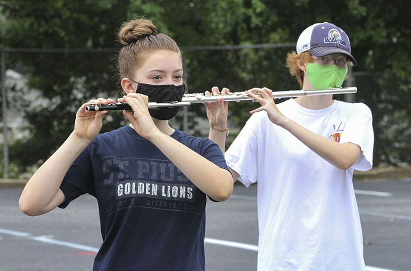 Freshman piccolo player Lauren Smith, left, and senior flute player Katie Fjelstul were two of the 20 brass and wind players on hand for the July 30 St. Pius X High School marching band sectional practice. It was the final day of band camp. Masks were the added accessory to this year's camp. They were only removed during actual playing and occasional water breaks. Photo By Michael Alexander