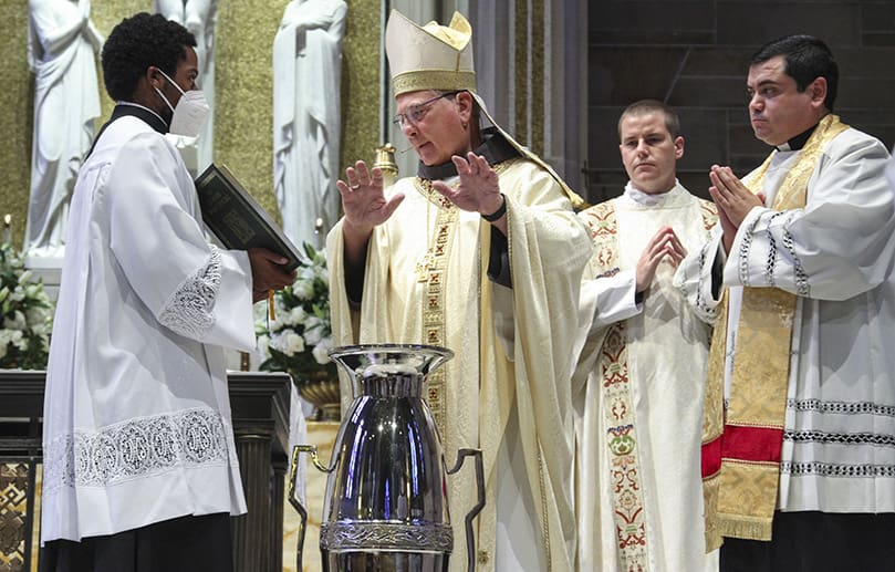 Standing on the altar at the Cathedral of Christ the King, Atlanta, for his first Chrism Mass as the archbishop of Atlanta, Archbishop Gregory J. Hartmayer, OFM Conv., second from left, conducts a blessing over the oil of the sick. Seminarian Avery Daniel is holding the Roman Pontifical as deacon of the altar Rev. Mr. Robbie Cotta, second from right, and master of ceremonies Father Gerardo Ceballos-Gonzalez look on. Photo By Michael Alexander