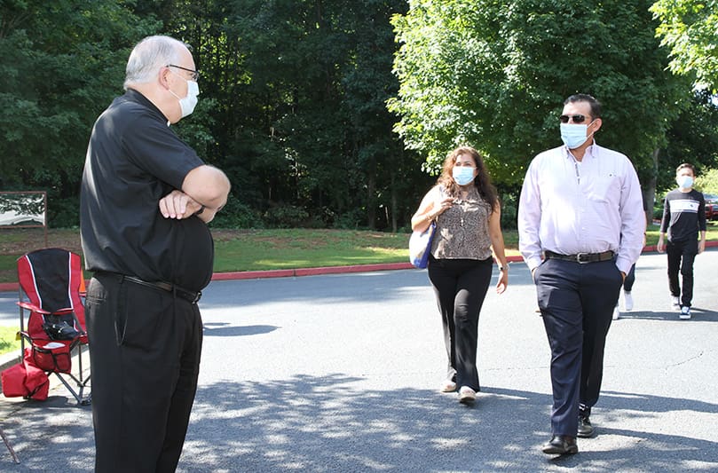 On the first Sunday of September, St. Thomas Aquinas Church pastor Msgr. Daniel Stack, left, greets families as they arrive for the 11 a.m. outdoor Mass. Photo By Michael Alexander