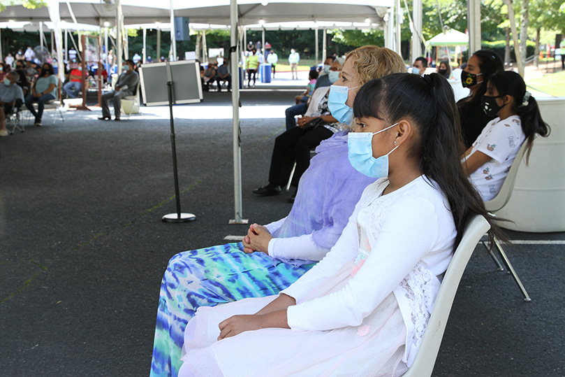 Maria Lopez and her daughter, Camila Angeles, listen to the homily, as they are seated under a tent, during the outdoor Spanish Mass on the first Sunday of September at St. Thomas Aquinas Church, Alpharetta. Photo By Michael Alexander