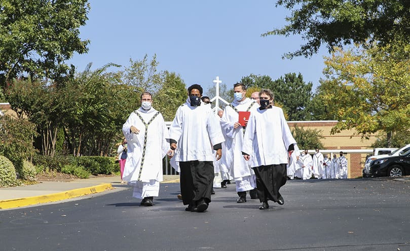 Seminarian and master of ceremony Avery Daniel, left, and the Office for Divine Worship’s Patricia DeJarnett, right, lead the procession of priests to St. Peter Chanel Church for the pallium Mass. Photo By Michael Alexander